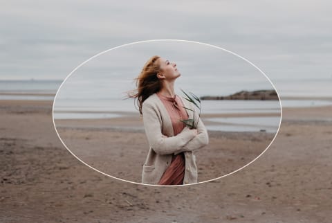 Pensive romantic adult woman with long red hair on the bay shore on a cloudy windy cold day