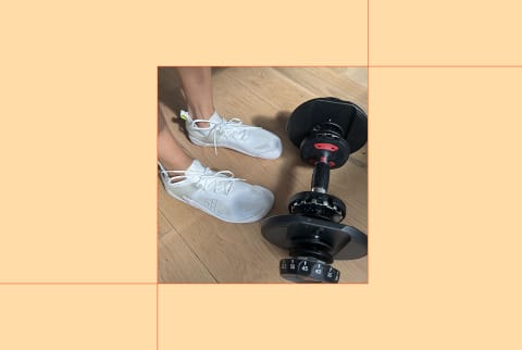 writer's feet in the vivobarefoot motus strength shoes in front of dumbbell on light orange background