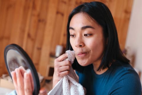 Young woman with acne looking in the mirror