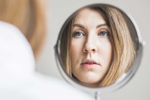 Woman looking at her face in the mirror