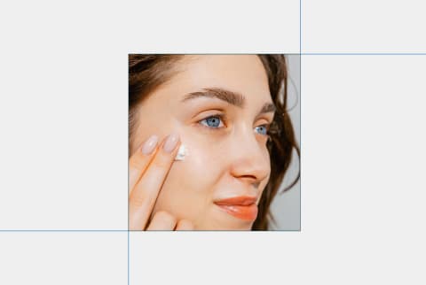 close-up image of woman putting cream on face on grey background