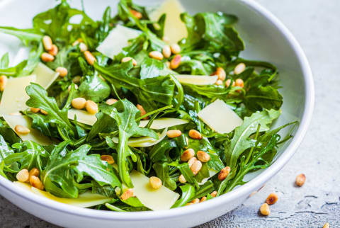 Arugula and parmesan salad with pine nuts in white bowl