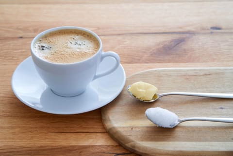 Bulletproof coffee with two spoons on a wooden table. Coconut oil and butter on the spoons.