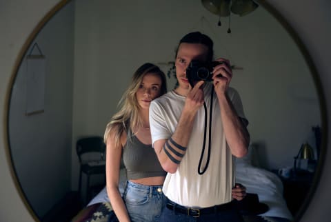 Couple taking a photo at home. They are standing in the bedroom taking a self portrait of each other through a round mirror hung on the wall.