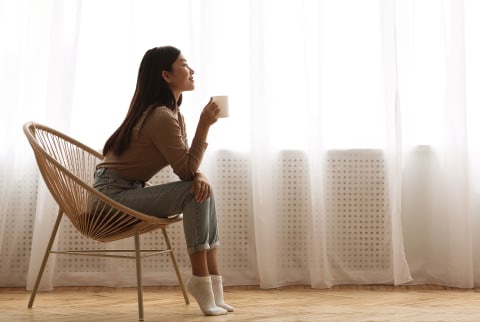 Young asian woman drinking a cup of coffee with curtains in the background
