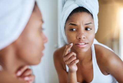 Young BIPOC woman looking at her skin and acne