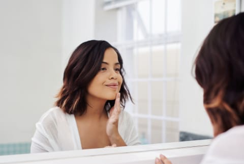 woman looking in mirror applying skincare