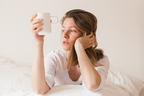 Tired Woman Sitting in Bed with Coffee Cup