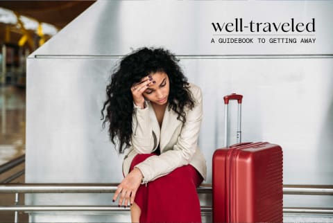 Woman with red carry on suitcase looking stressed at airport