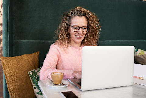 blonde curly-haired woman with glasses looking at her laptop