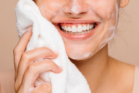 Portrait of a young woman with great skin, taking of face foam with white towel