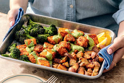 Woman in denim shift holding sheet pan with broccoli, salmon and potatoes