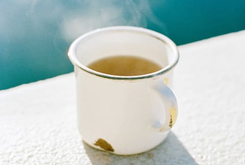 Hot green tea in a white metal mug with steam rising