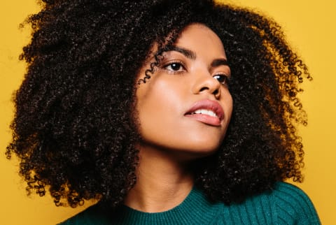 Young Woman with Natural Hair and Glowing Skin on a Yellow Background