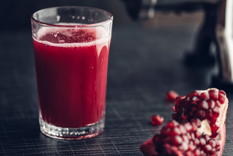Glass of pomegranate juice with juicer in background and a slice of the fruit Glass of pomegranate juice with juicer in background and a slice of the fruit