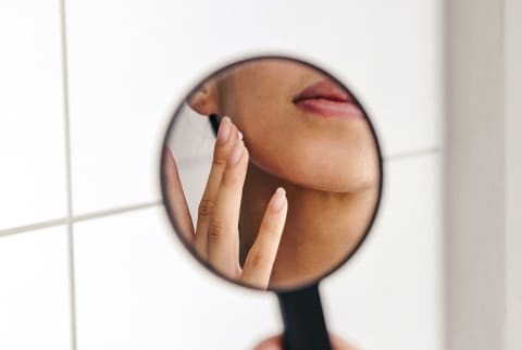 Woman Applying Skin Cream in a Handheld Mirror