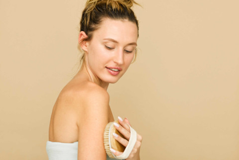 Woman wrapped in towel uses a drybrush on upper arm Woman wrapped in towel uses a drybrush on upper arm