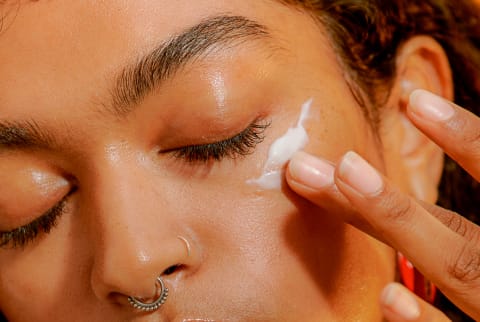 Young woman applying moisturizer to her face