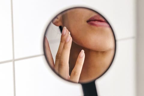 Woman Applying Skin Cream in a Handheld Mirror