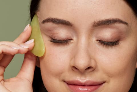 a woman using a gua sha stone on a green background 