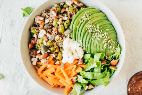 Overhead of a grain bowl with avocados, seeds, carrots and other ingredients