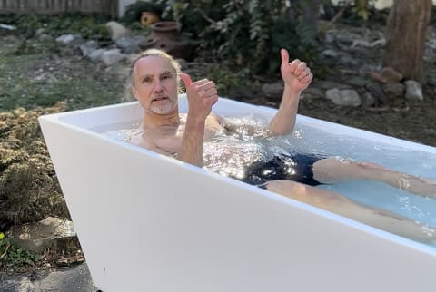 Tester sitting in the plunge cold plunge tub with thumbs up in his home garden 