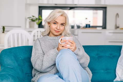 Beautiful blond woman spending her day off at home, sitting on the couch, drinking coffee