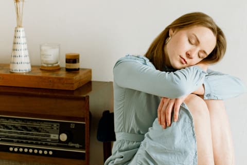 woman in a blue dress sitting at home and hugging her knee