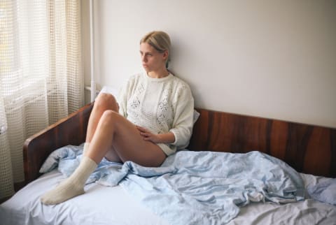blonde woman sitting on bed looking sad