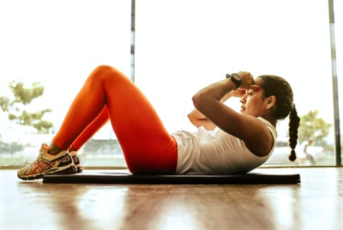 Woman doing crunches on a yoga mat in a well lit studio