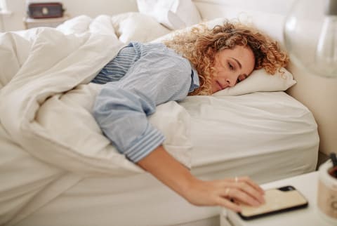 Woman waking up in the morning and reaching for her phone