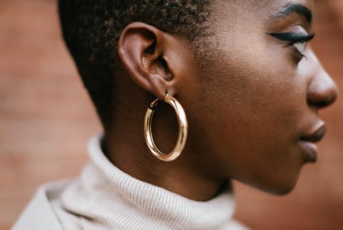 Side view of stylish African American female with shiny golden earring on blurred background of building on city street