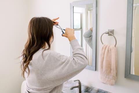Woman Trimming Her Bangs in the Bathroom Mirror