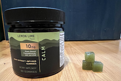 Charlotte's Web Calm CBD Gummy in container next to stack of three green gummies
