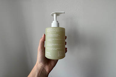 Act+Acre Cold Processed Curl Cleanse held in hand against wall back of bottle