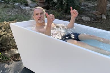 man in water of cold plunge tub with thumbs up with tub outdoors