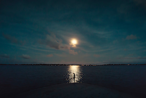 Young female silhouete at the shore with the reflected light of the moon on the sea