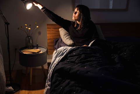 Woman sitting in bed turns out lamp to go to sleep Woman sitting in bed turns out lamp to go to sleep