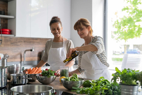 Two woman cooking in a kitchen with fruits and veggies Two woman cooking in a kitchen with fruits and veggies