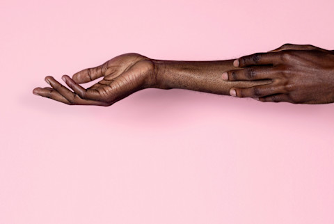 Black person running their fingertips against their outstretched arm against a pink background. Black person running their fingertips against their outstretched arm against a pink background.