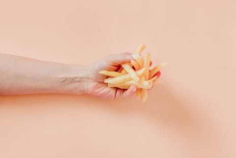 forearm with handful of french fries over peach background