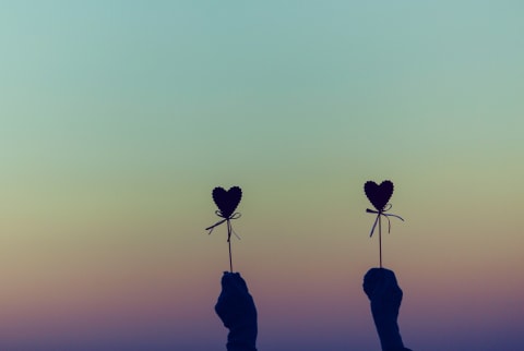 silhouette of two hands holding heart craft in front of sunset