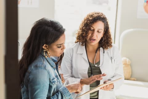 A female doctor discusses a young patient's diagnosis with the patient's mother. They are reviewing the patient's test resutls.