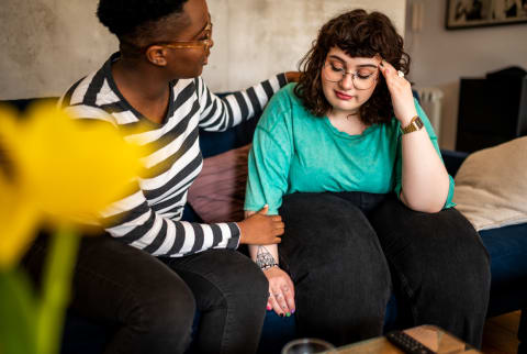 two women sitting at a couch, one looking somber