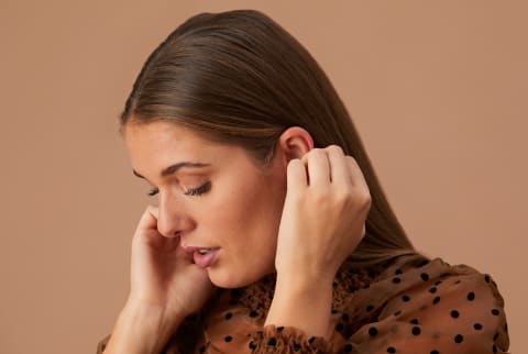 woman putting her hair behind her ears on brown background