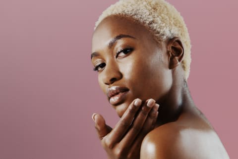 black woman with blonde hair and glowing skin on a pink background