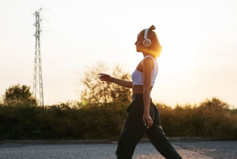 Woman walking on road at sunset wearing headphones