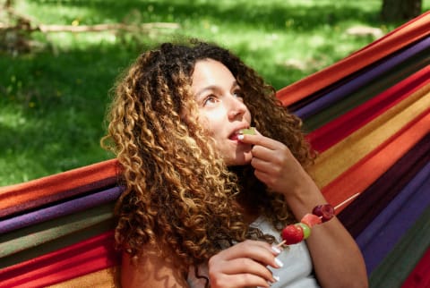 Curly haired woman in a hammock eating a snack