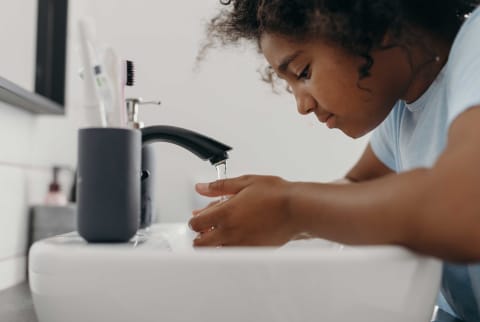 Young black girl washing her face over the sink