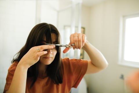woman cutting her bangs in the mirror